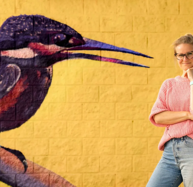 Jolien met gele achtergrond-4 SEO-tekstschrijver Jolien voor gele muur met een geschilderde vogel.